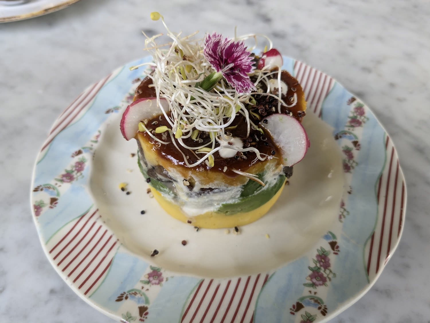 Causa at Raw Café in Lima: layered potato topped with sprouts and an edible flower, on a patterned plate.